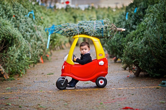 child driving plastic toy car with christmas tree on top