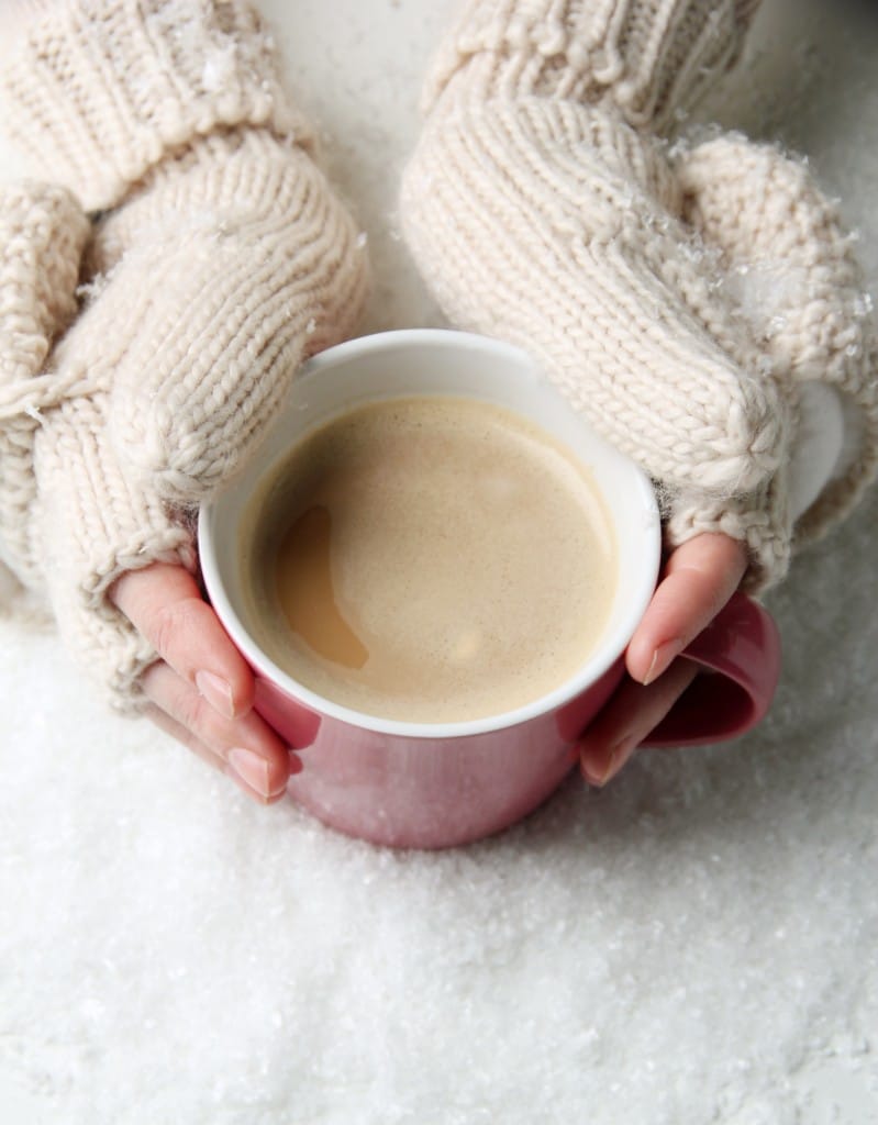 Two hands in winter gloves holding a mug of hot cocoa