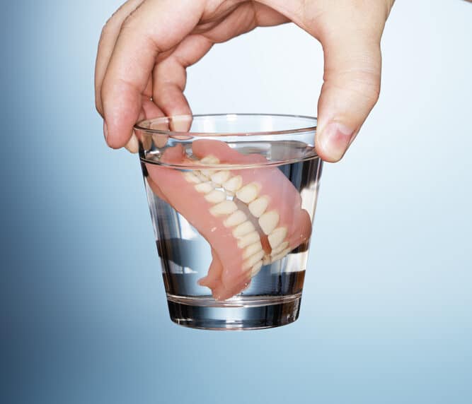 man holding dentures in a glass of water