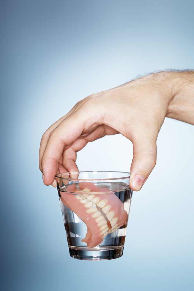 man holding dentures in a glass of water