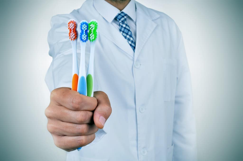 Dentist holding three multicolored toothbrushes
