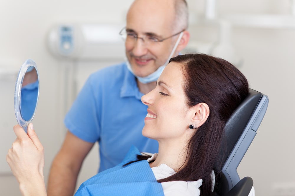 dentist and uninsured patient looking at teeth in the mirror