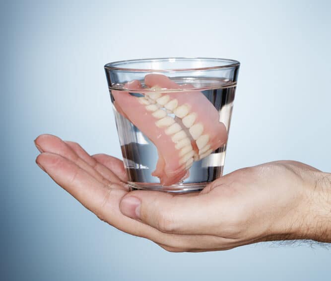 person holding a glass with dentures inside