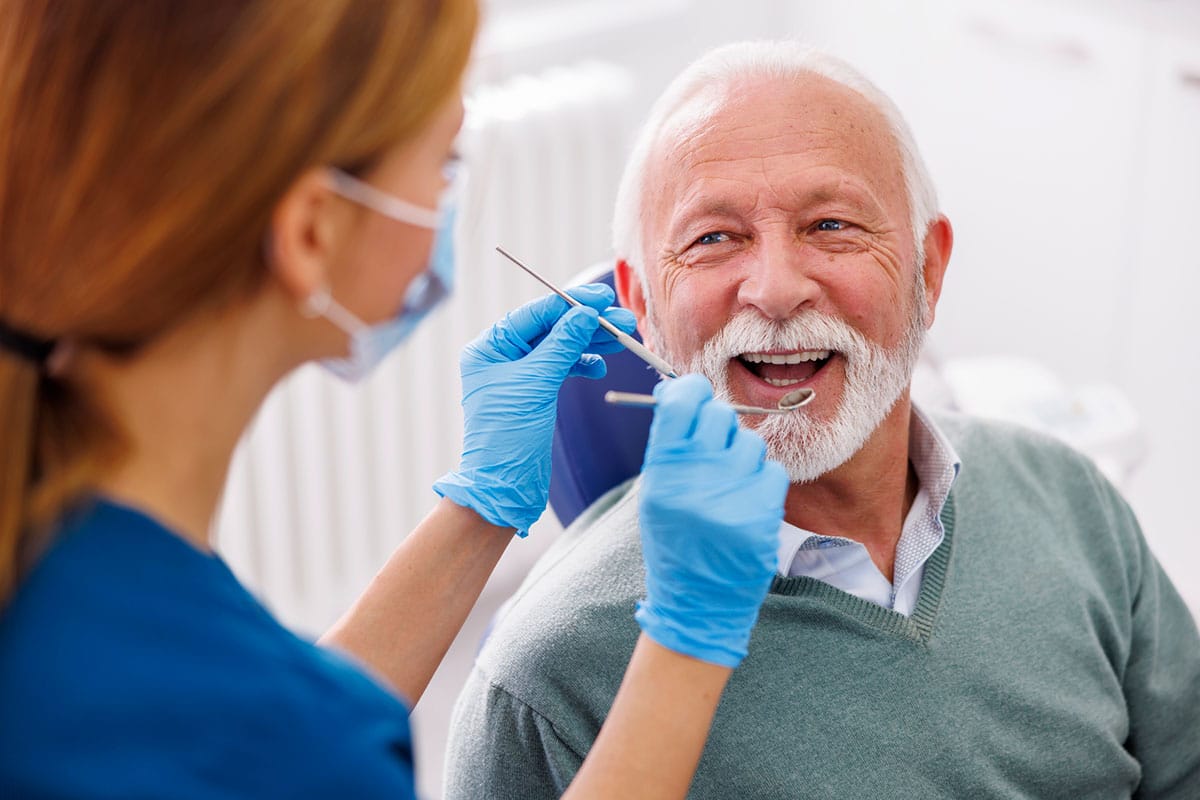 senior gentleman at the dentist, smiling at the female dental hygienist or dentist who is examining his teet