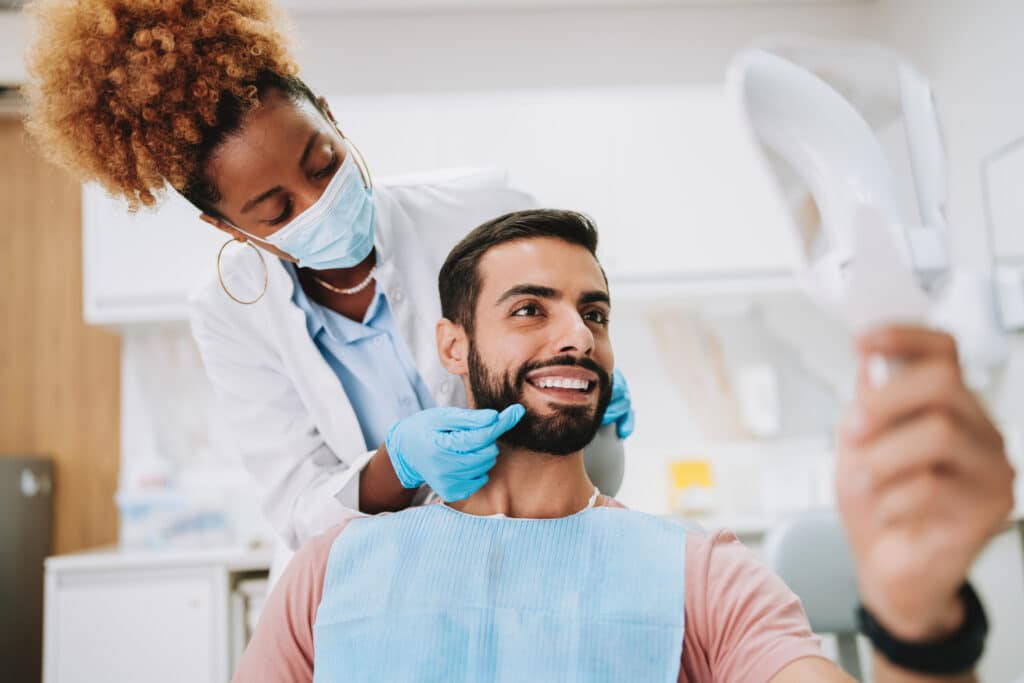 Man dental treatment with woman dentist looking in mirror
