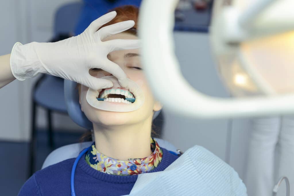 woman at dentist giving a young female patient in-office whitening treatment.