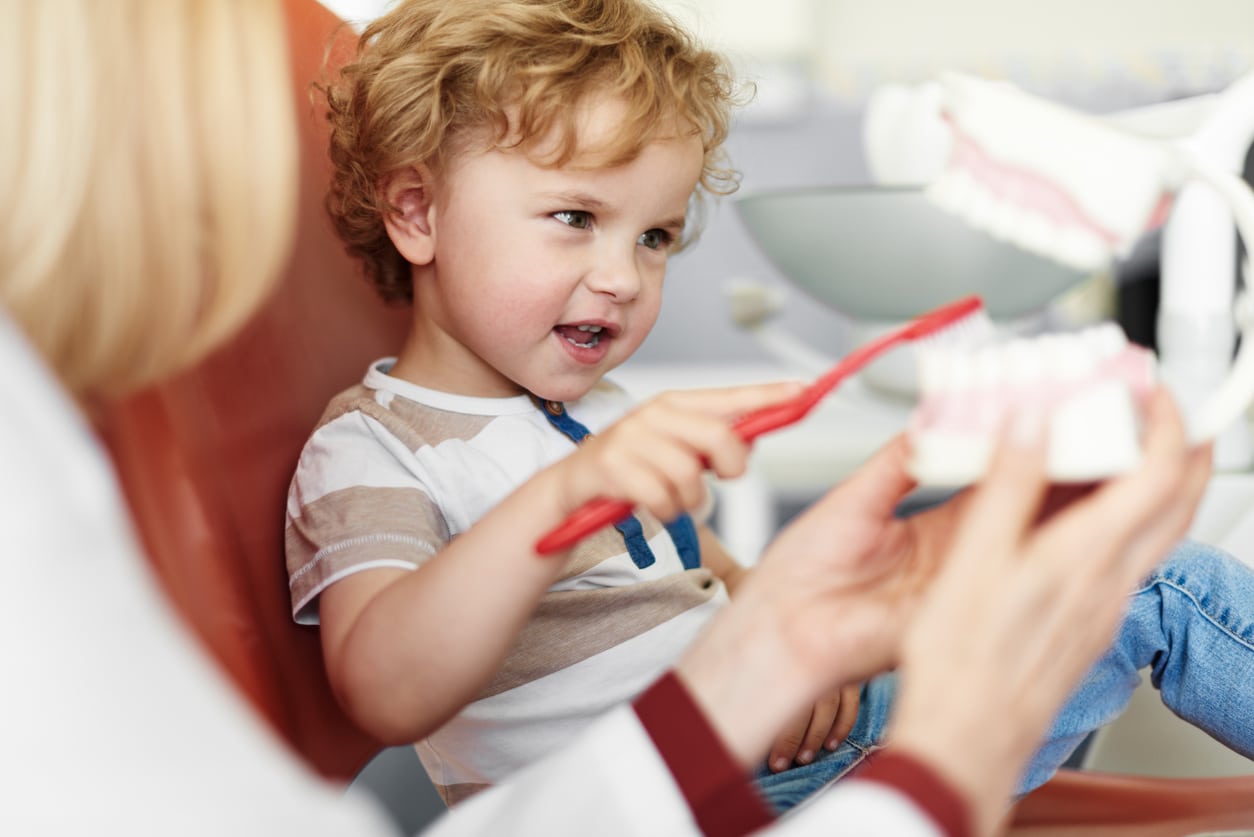 Curious little boy brushing teeth on dental model while he sitting on dental chair, learning dental habit concept