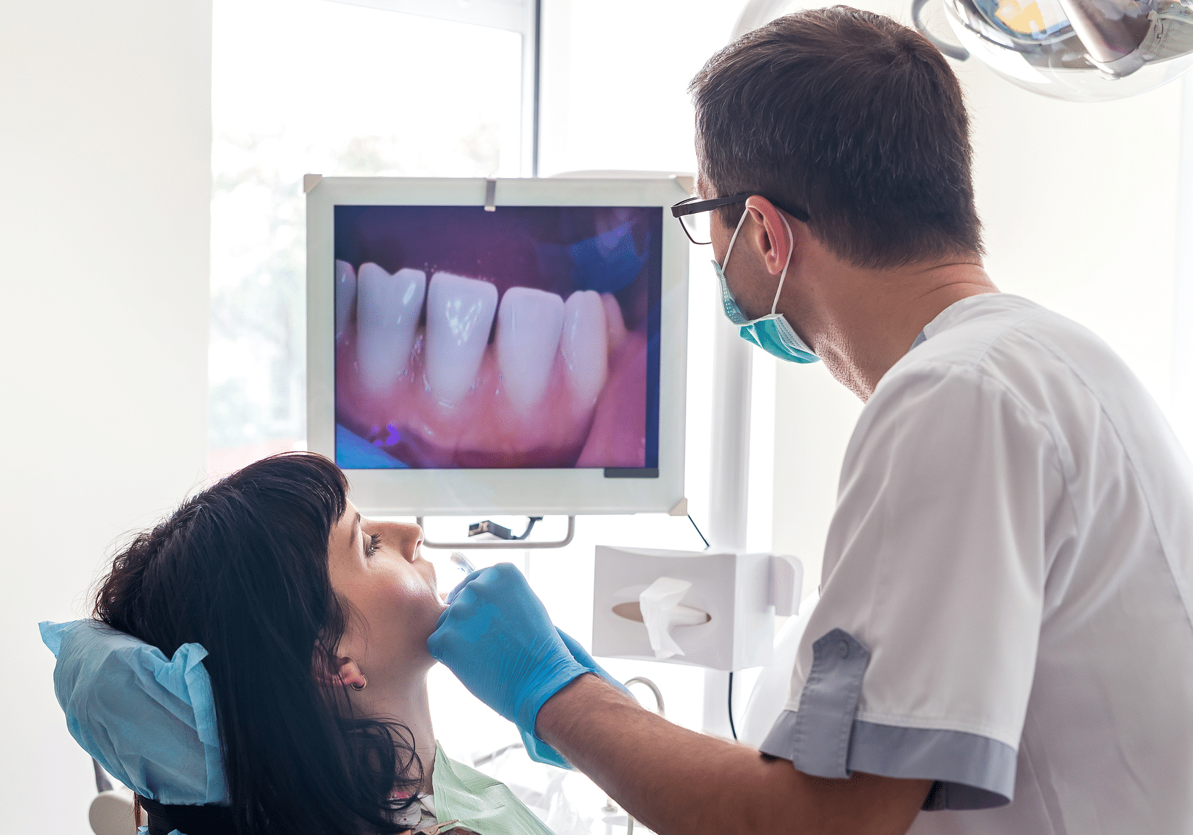 Dentist checking a patient's teeth using an intraoral camera, with the image displayed on a screen for them to view
